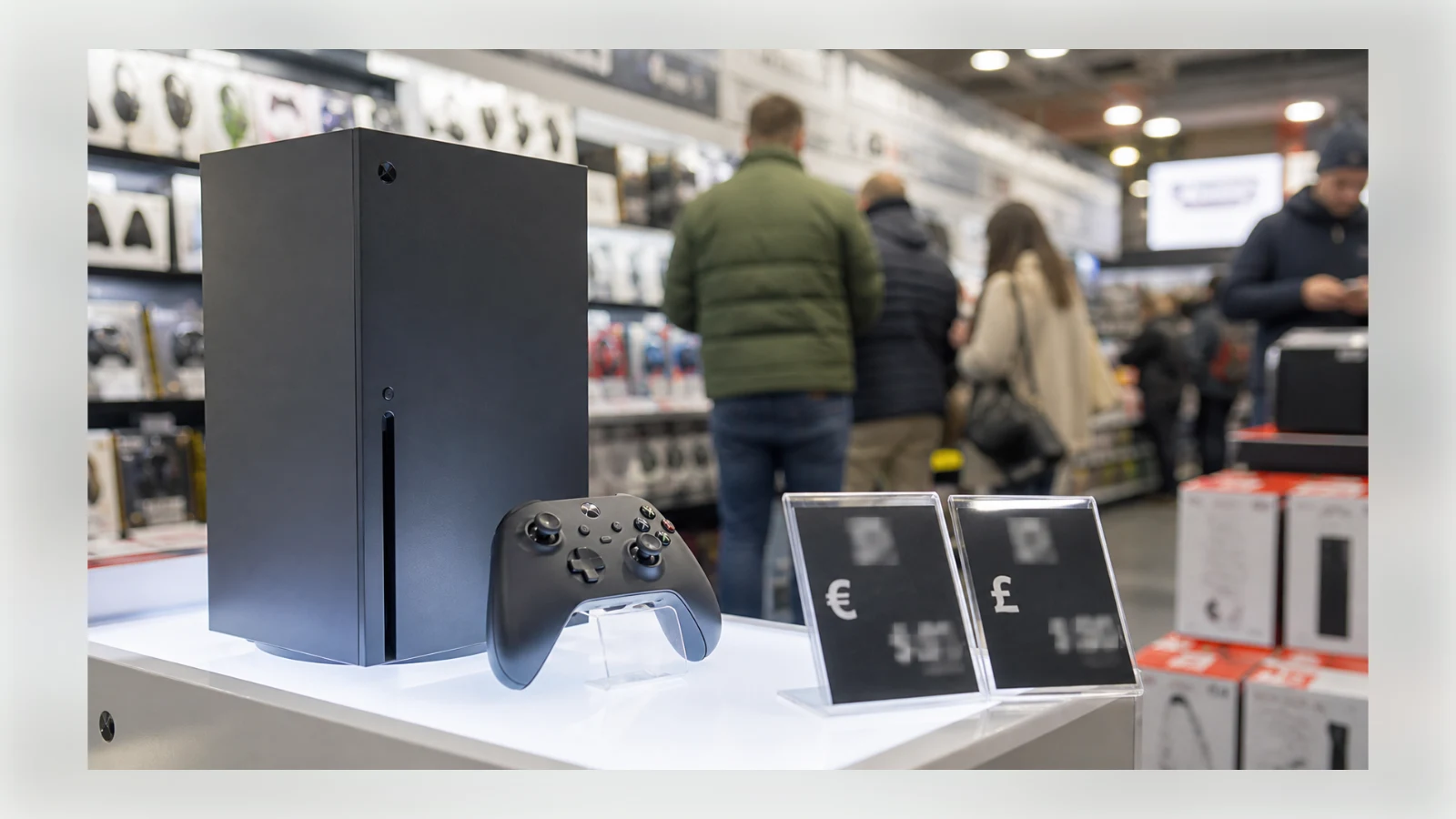 An unbranded game console displayed beside euro and pound price cards in a retail store.