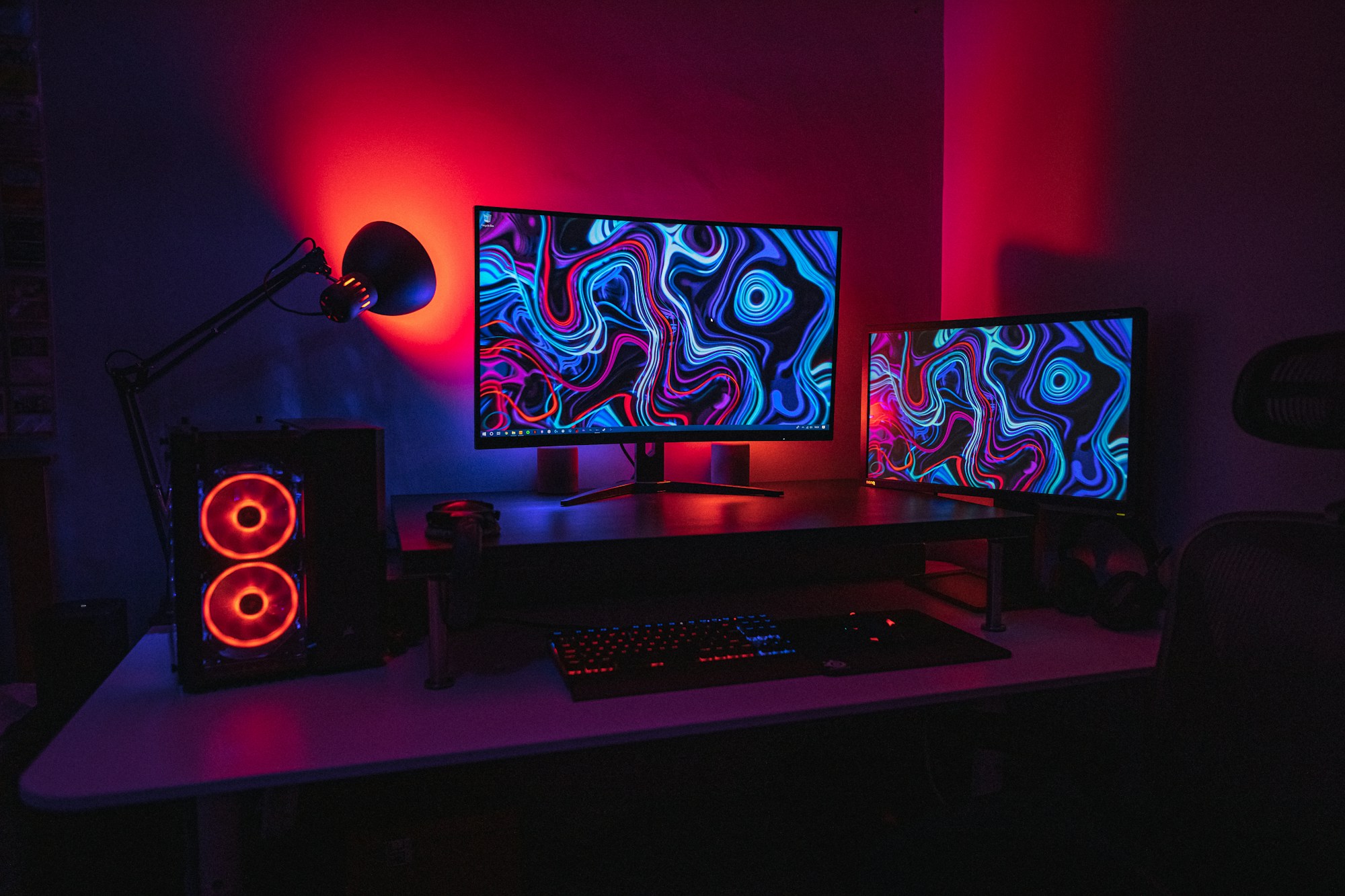 Two gaming monitors in a red-and-blue illuminated desktop setup. Photo by Jack B on Unsplash; representative image.